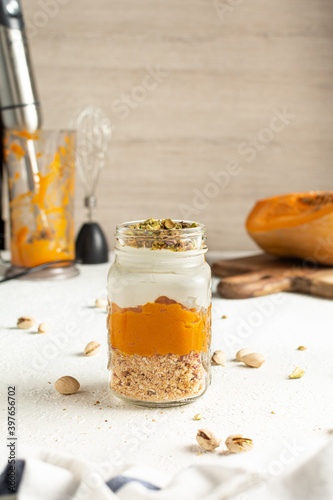 Pumpkin parfait with pistachios in Glass Mason Jar Mugs, blender and pumpkin in the background