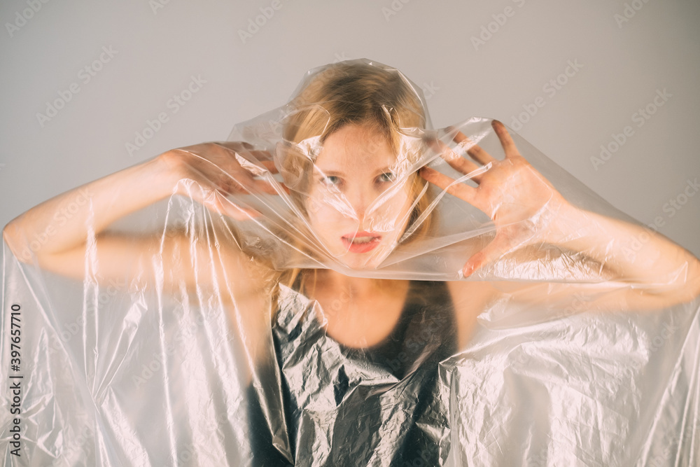 Naklejka premium Stop violence. Defocused art portrait. Female rights. Woman protection. Annoyed disturbed woman trapped in transparent polyethylene film isolated on gray background out of focus.