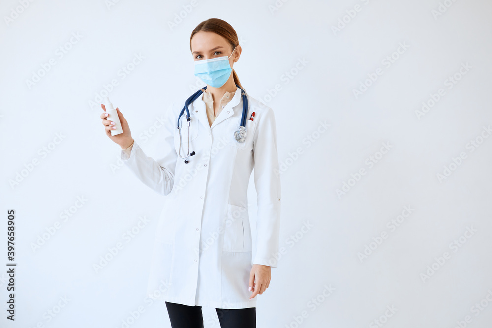 Waist up portrait of beautiful nurse posing confidently while standing with stethoscope and hand sanitizer against white wall Waist up portrait of beautiful nurse posing confidently while standing with stethoscope and hand sanitizer against white wall