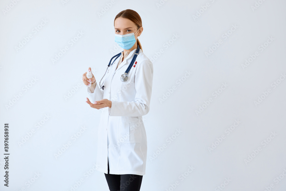 Waist up portrait of beautiful nurse posing confidently while standing with stethoscope and hand sanitizer against white wall Waist up portrait of beautiful nurse posing confidently while standing with stethoscope and hand sanitizer against white wall