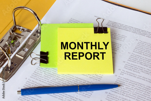 Text Monthly Report on a yellow sticker that is in a folder with documents and a blue pen