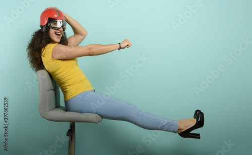 Woman with red helmet thinks to drive a fast car. cyan background.
