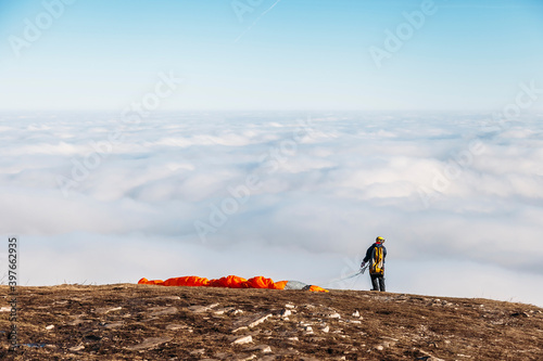 paraglider prepares to jump into sky from the top of a mountain above the clouds