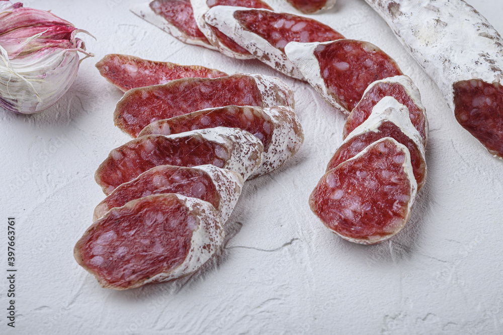 Dry cured fuet salami sausage slices with herbs on white surface