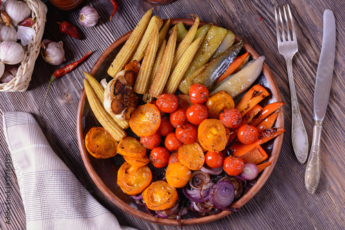 Appetizing grilled vegetables next to spices, fork and knife on a wooden table, top view