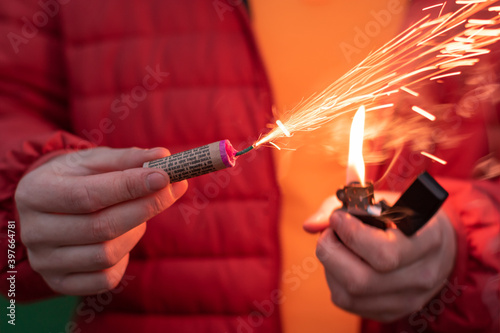 Man in Red Jacked Lighting Up Firecracker in his Hand Using Gasoline Lighter. Guy Getting Ready for New Year Fun with Fireworks or Pyrotechnic Products