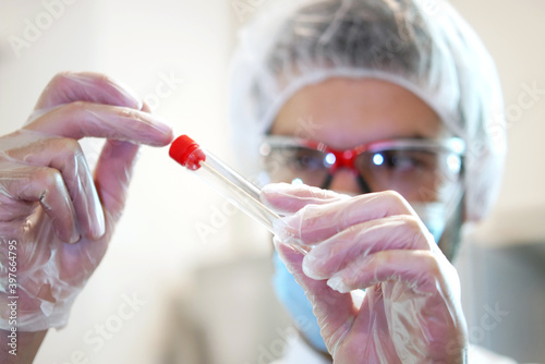 Young attractive caucasian man scientist researching in the hospital laboratory  looks at the sample of throat and nose swab  close up of doctors face and hand with test tube 