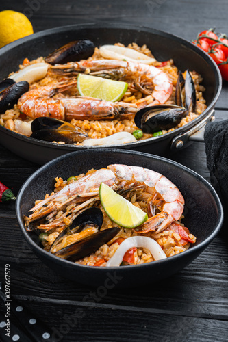 Valenciana seafood paella in bowl and frying pan on black wooden planks