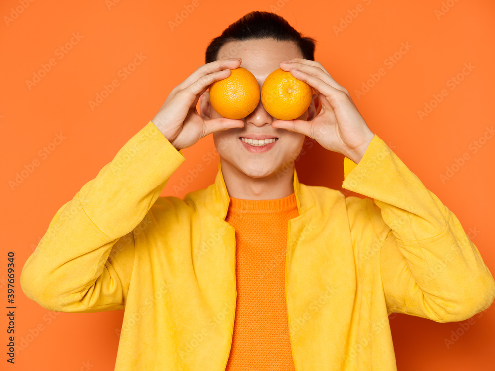 Asian man with oranges before eyes yellow jacket isolated background Asian man with oranges before eyes yellow jacket isolated background