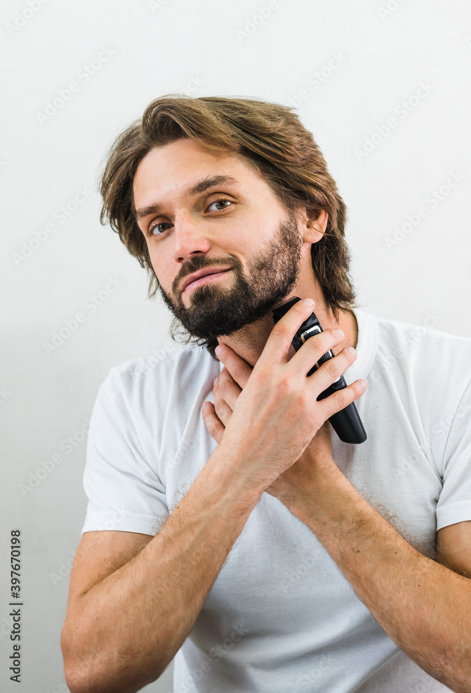 Man shaving his beard in the mirror with electric razor. Man with beard. Shaving his beard in the mirror with electric razor, indoors, coronavirus isolation concept and lockdown, new normal. Man shaving his beard in the mirror with electric razor. Man with beard. Shaving his beard in the mirror with electric razor, indoors, coronavirus isolation concept and lockdown, new normal.