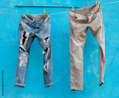 Two pairs of jeans drying against a blue wall