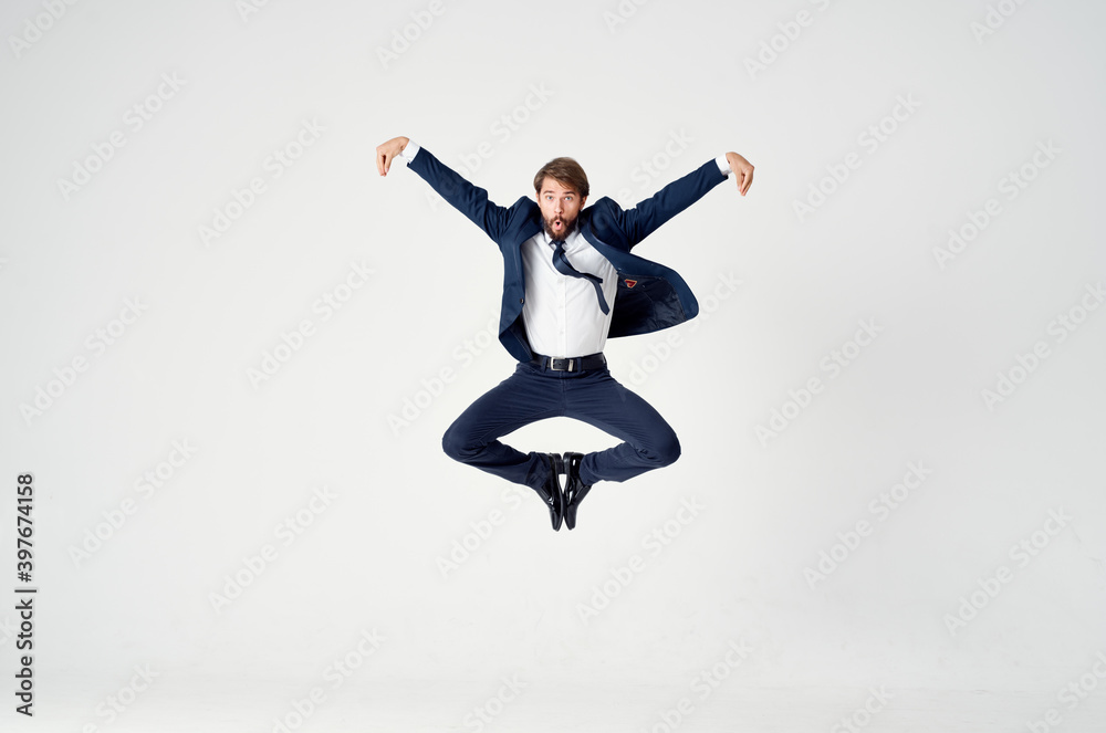 Energetic business man in a blue suit jumps up on a light background success