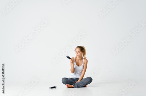 an athletic woman in a bright room sits on the floor and looks at dumbbells 