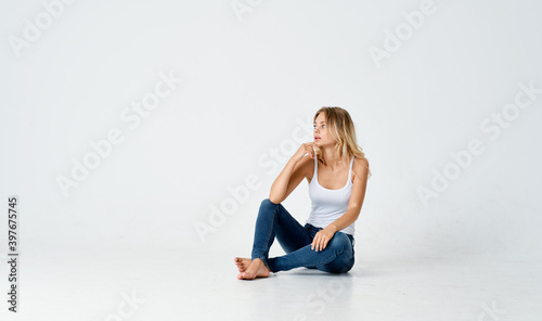 woman sits on the floor on a light background in jeans and a t-shirt 