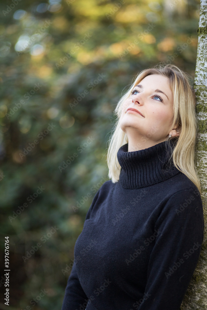 Serious young girl dressed in turtleneck is posing in the autumn park looking up. Vertically. Serious young girl dressed in turtleneck is posing in the autumn park looking up. Vertically.