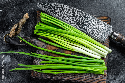 Fresh green onions on a cutting board. Black background. Top view
