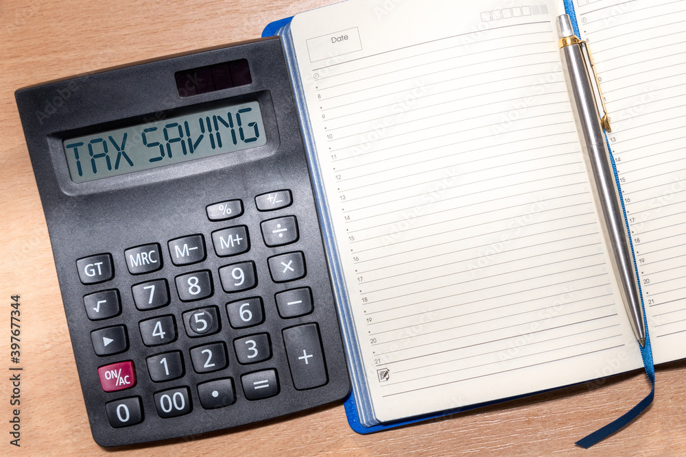 Calculator with the text Tax Saving. Calculator, Notepad and pen on a wooden table. Business, financial concepts. Calculator with the text Tax Saving. Calculator, Notepad and pen on a wooden table. Business, financial concepts.