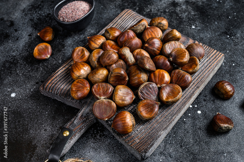 Raw chestnuts on a wooden cutting board. Black background. Top view