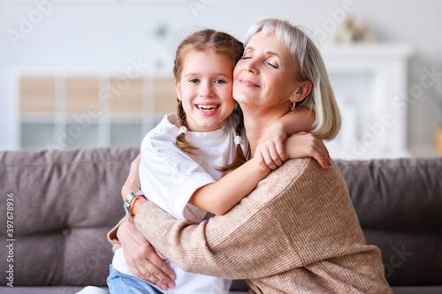 Slika na platnu Happy grandmother and granddaughter hugging on sofa.
