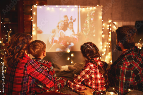 family mother father and children watching projector, film, movies with popcorn in christmas evening at home.