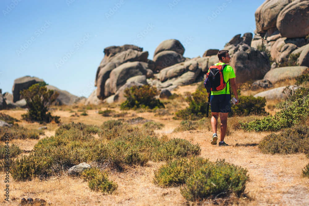 Naklejka premium Hiker man walks along a dirt road towards the rocks on summer