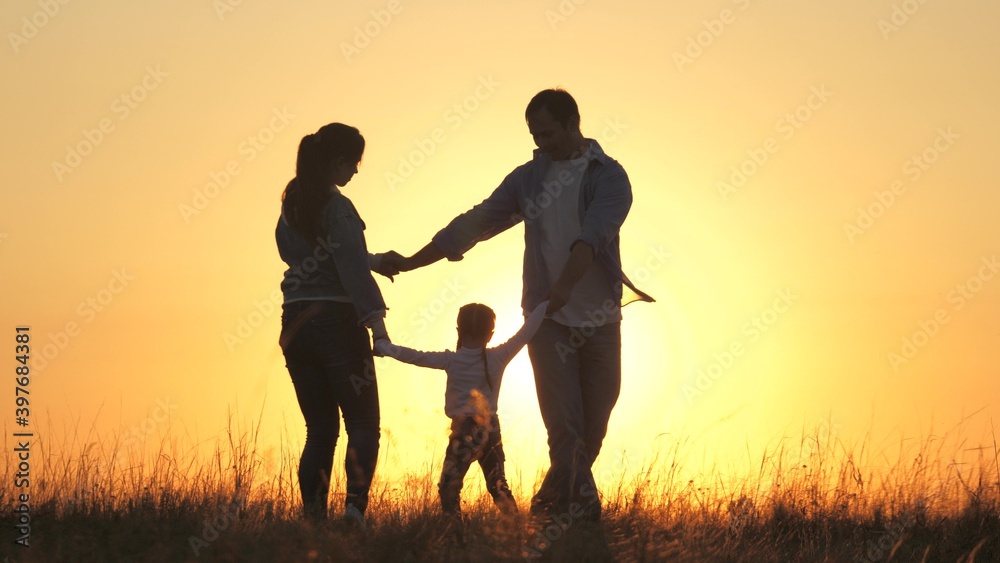young mom, dad with a healthy daughter dance in a circle under warm sun, have fun in field. happy family, holding hands, plays in the park on grass, at sunset. Family and childhood concept.
