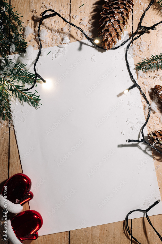 Christmas background from a table of snow-covered wooden boards, decorated with spruce legs, cones and a garland, and a white sheet of paper for congratulations. Flat lay, top view