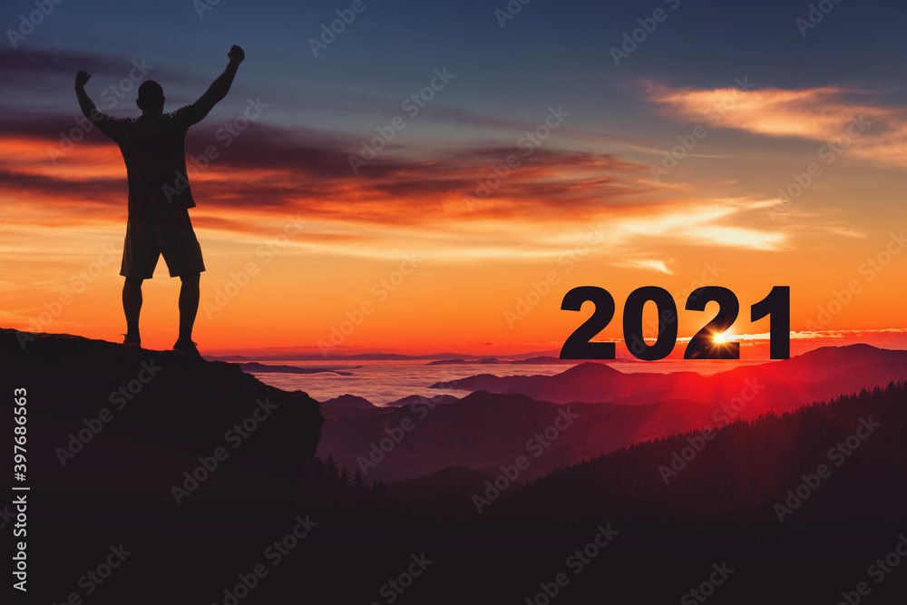 Man silhouette on the mountain top watching the sunrise and 2021 years while celebrating Man silhouette on the mountain top watching the sunrise and 2021 years while celebrating