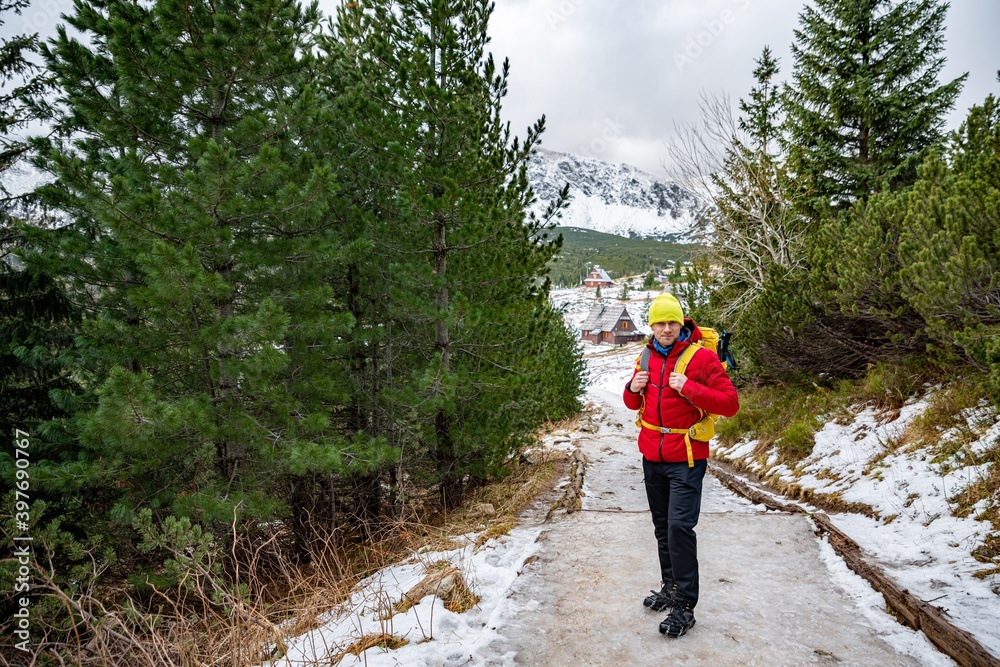 Smiling Tourist in a red down jacket, yellow hat and yellow backpack spends his free time in the mountains.