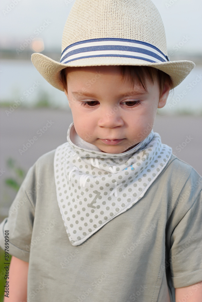 Stylish, happy child walks in the summer park by the river in a straw hat