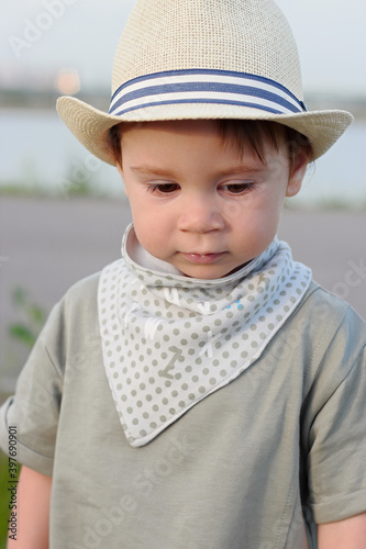 Stylish, happy child walks in the summer park by the river in a straw hat