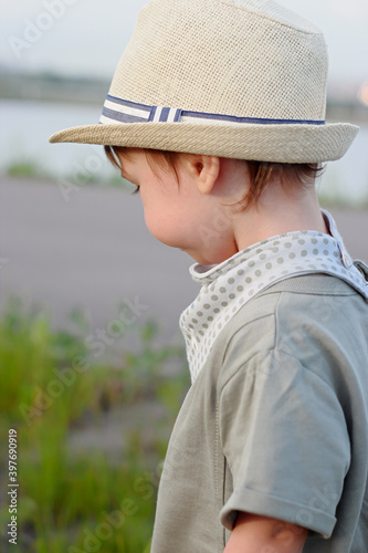 Stylish, happy child walks in the summer park by the river in a straw hat