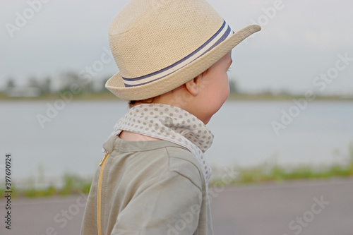 Stylish, happy child walks in the summer park by the river in a straw hat
