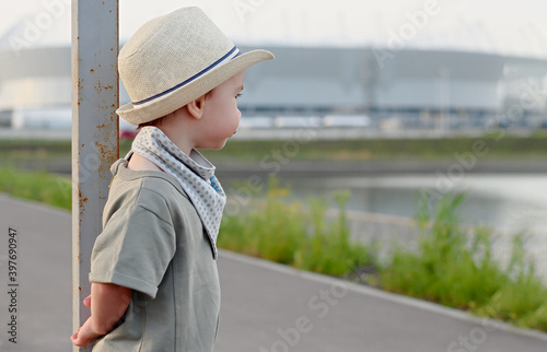 Stylish, happy child walks in the summer park by the river in a straw hat