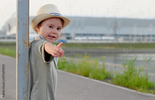 Stylish, happy child walks in the summer park by the river in a straw hat