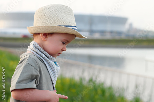 Stylish, happy child walks in the summer park by the river in a straw hat