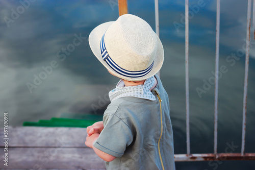 Stylish, happy child walks in the summer park by the river in a straw hat