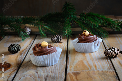 Delicious muffins with chocolate cream and nuts on a wooden table with pine cones and spruce branches. Selective focus