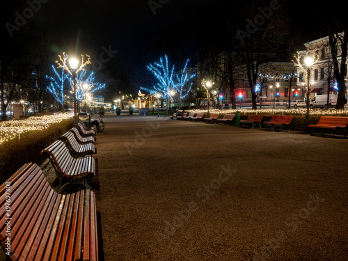 A beautiful view of a public park with Christmas lights and decorations. A row of wooden beches. photo