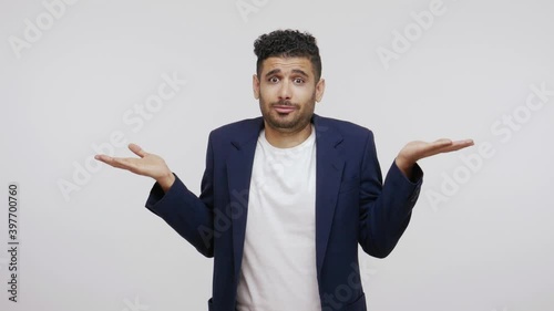 Puzzled confused man with beard in business suit shrugging shoulders and throwing up hands, uncertain about information, dont know facts. Indoor studio shot isolated on gray background