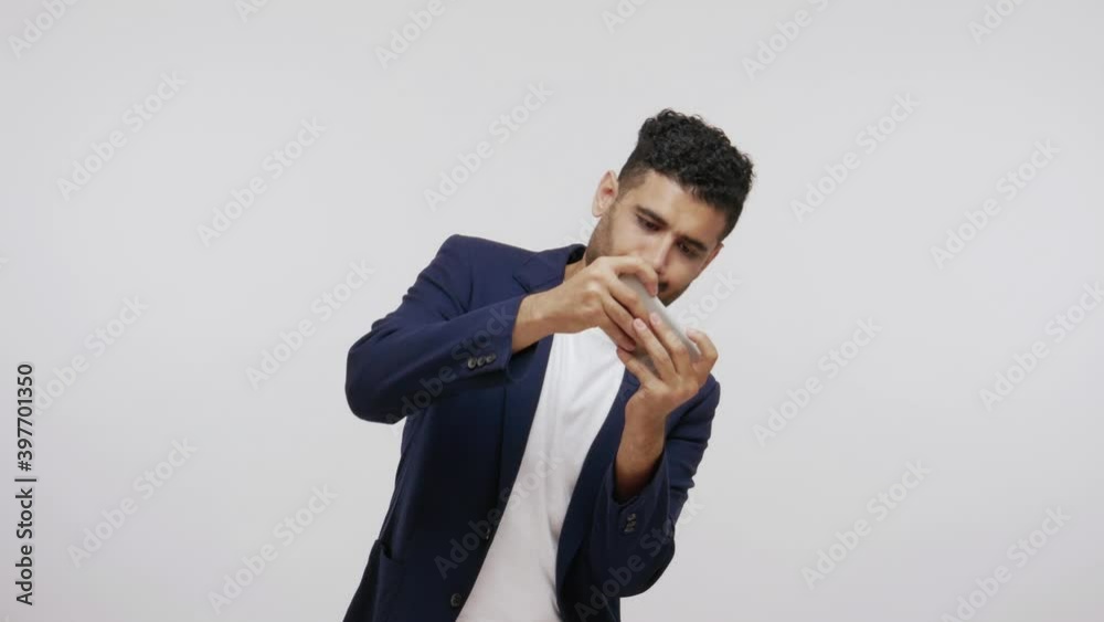 Infantile bearded man in business suit playing action games on smartphone, virtual reality, gaming. Indoor studio shot isolated on gray background Infantile bearded man in business suit playing action games on smartphone, virtual reality, gaming. Indoor studio shot isolated on gray background