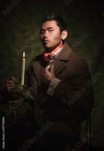 This image is a painterly style victorian portrait of a a well dressed asian man, holding an antique burning candle and fixing his suit as he looks towards the viewer.  photo