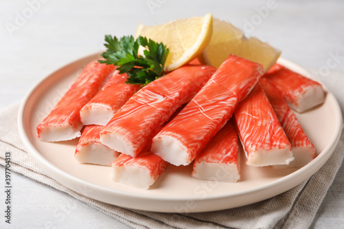 Plate of fresh crab sticks with lemon on white table, closeup