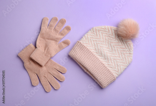 Woolen gloves and hat on violet background, flat lay