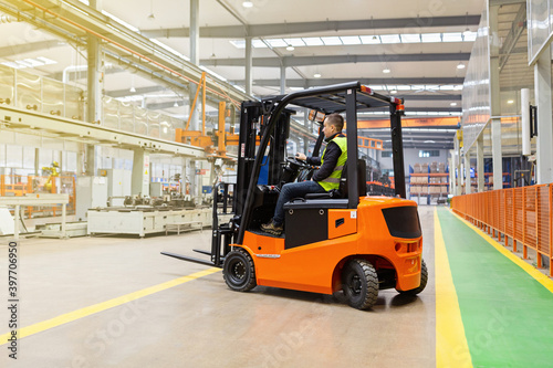 Storehouse employee in uniform working on forklift in modern automatic warehouse. Boxes are on the shelves of the warehouse. Warehousing, machinery concept. Logistics in stock. © Алина Бузунова