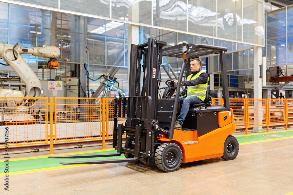 Storehouse employee in uniform working on forklift in modern automatic warehouse. Boxes are on the shelves of the warehouse. Warehousing, machinery concept. Logistics in stock.