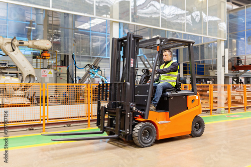 Storehouse employee in uniform working on forklift in modern automatic warehouse. Boxes are on the shelves of the warehouse. Warehousing, machinery concept. Logistics in stock. photo