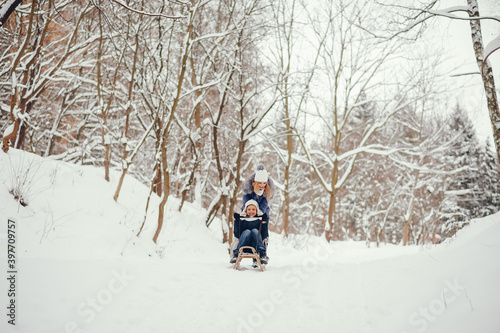 Beautiful mother in a blue jacket. Family sledding in a winter park. Little boy in a cute hat © prostooleh