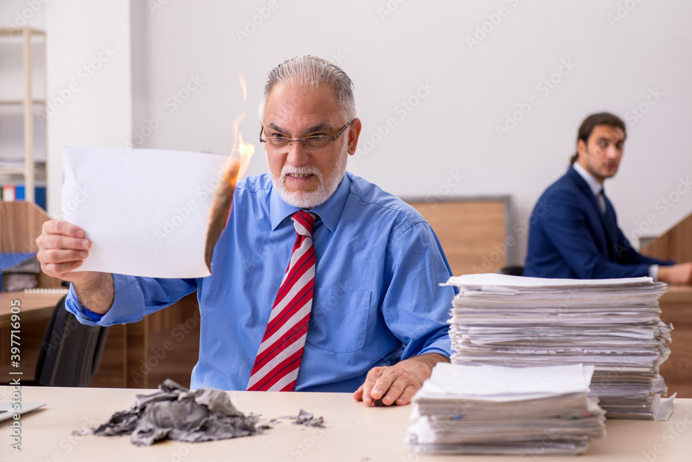 Young male employee and old boss burning papers at workplace