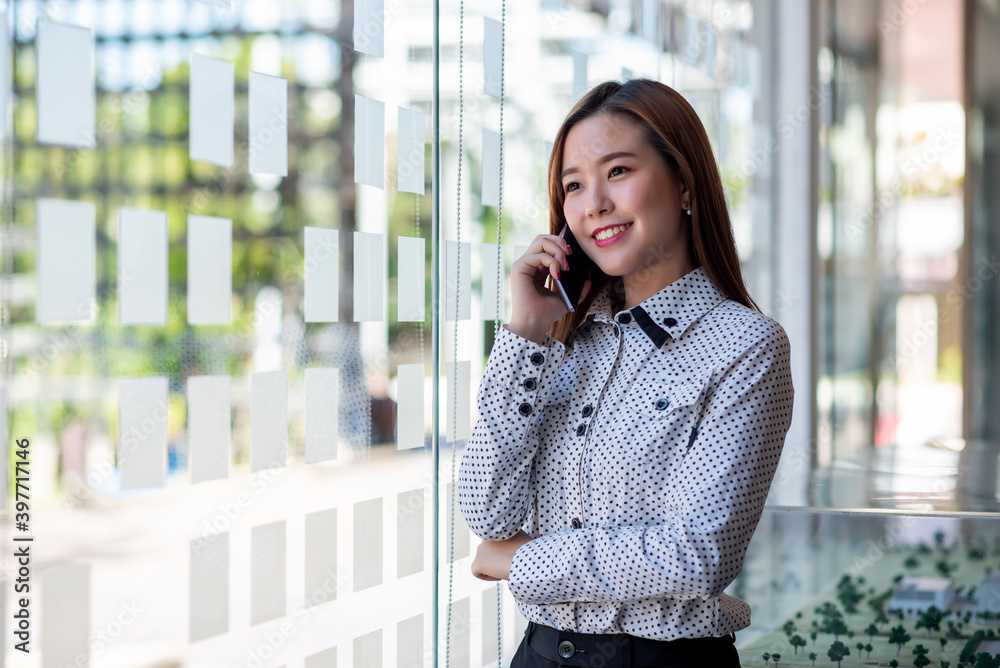 Fototapeta premium Attractive young asian business woman standing talking on the mobile phone in the office.